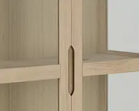 Nærbillede af en skabslåge lavet af lyst træ med et lodret, ovalformet indfræset greb. Skabet har en glat overflade og rene linjer, og der ses en vandret hylde indeni. Designet er minimalistisk og moderne.