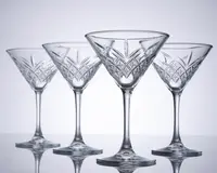 Sæt med fire klare krystalglas med bred, lav skål og lang stilk. Hvert glas har et indviklet slebet mønster med geometriske og vifteformede detaljer omkring skålen, hvilket giver dem et elegant og klassisk udseende. Glassene har en solid fod og er arrangeret på række, så det detaljerede håndværk fremhæves.