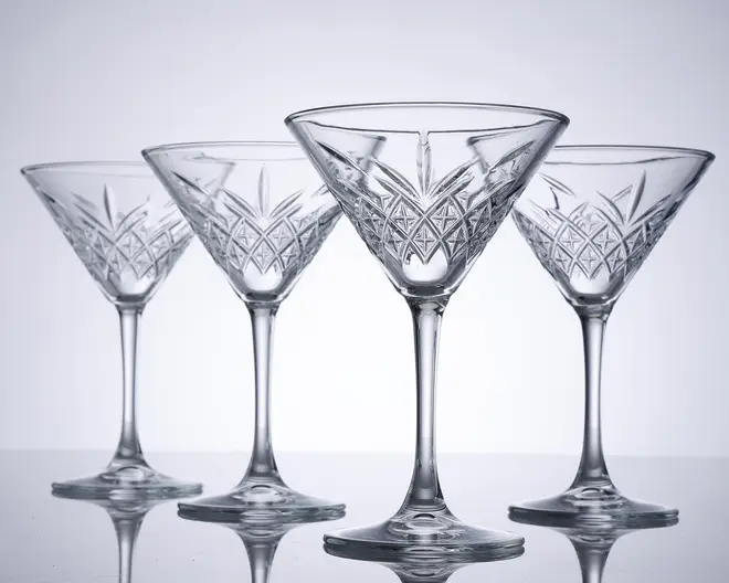 Sæt med fire klare krystalglas med bred, lav skål og lang stilk. Hvert glas har et indviklet slebet mønster med geometriske og vifteformede detaljer omkring skålen, hvilket giver dem et elegant og klassisk udseende. Glassene har en solid fod og er arrangeret på række, så det detaljerede håndværk fremhæves.