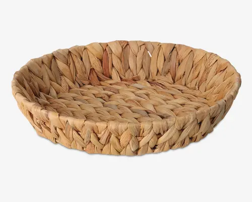 Rund, lav kurv fremstillet af tykke, tæt flettede naturfibre. Kurven har en solid struktur med et flettet mønster, hvilket giver et rustikt og håndlavet udtryk. Kanten er let forhøjet, og farven er en blanding af lyse og mellembrune nuancer, som fremhæver det naturlige materiale.