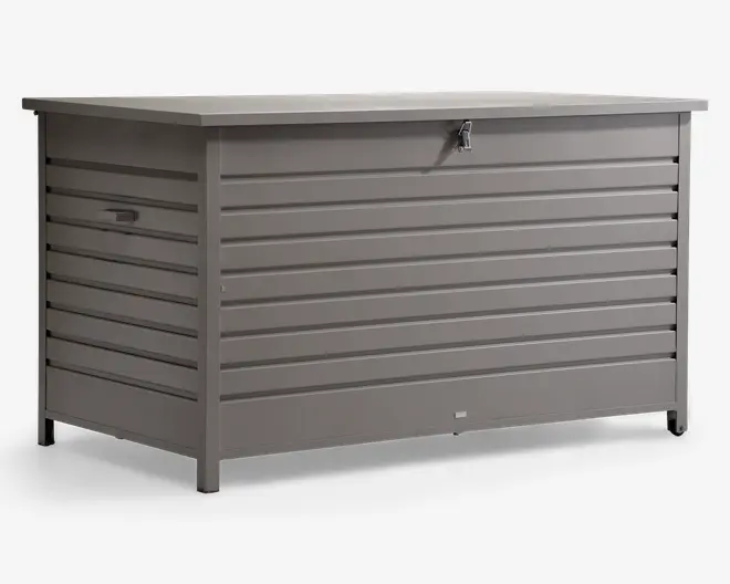 Stor rektangulær opbevaringsboks lavet af metal med vandrette lameller på alle sider. Boksen er malet i mat grå og har et fladt låg, der rager lidt ud over kanterne, samt en låsbar haspe foran for ekstra sikkerhed. Der er solide håndtag på siderne, så den er nem at løfte og flytte. Boksen står på korte ben, som løfter den lidt fra jorden.