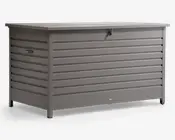 Stor rektangulær opbevaringsboks lavet af metal med vandrette lameller på alle sider. Boksen er malet i mat grå og har et fladt låg, der rager lidt ud over kanterne, samt en låsbar haspe foran for ekstra sikkerhed. Der er solide håndtag på siderne, så den er nem at løfte og flytte. Boksen står på korte ben, som løfter den lidt fra jorden.