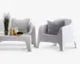 Moderne udendørs siddegruppe bestående af en hvid lænestol og en matchende to-personers sofa, begge med glatte, buede linjer og et minimalistisk design. Sættet inkluderer et lavt, rektangulært sofabord. Lænestolen og sofaen har hver en grå eller stribet pude for ekstra komfort. På bordet står en potteplante, en glaskande med citronskiver, to glas med gult mønster og et træfad med druer, hvilket skaber et friskt og indbydende udtryk.