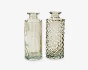 To klare glasflasker med brede, flade åbninger og cylindrisk form. Flasken til venstre har lodrette rillede linjer, der løber fra top til bund og giver en tekstureret overflade. Flasken til højre har et diamantmønstret, quiltet tekstur over hele overfladen. Begge flasker har tykke, solide bunde og et vintage-inspireret design.