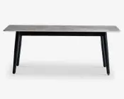 Rektangulært bord med en lysegrå bordplade med træstruktur og fire skråtstillede sorte ben. Designet er minimalistisk og moderne med rene linjer og en glat overflade. Benene er let tilspidsede, hvilket giver bordet et elegant udtryk.