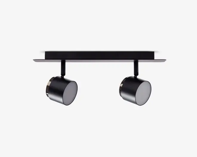 Moderne loftmonteret armatur med to justerbare cylindriske spotlys, der er fastgjort til en rektangulær base. Armaturet har en mat sort finish, hvilket giver det et stilrent og moderne udseende. Hver spot kan rettes individuelt for at belyse bestemte områder, hvilket gør det velegnet til accent- eller arbejdsbelysning.
