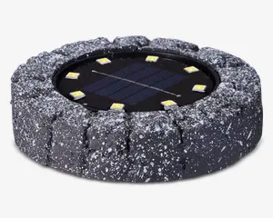 Rund udendørslampe med et robust, stenlignende ydre i mørkegrå med hvide pletter. I midten sidder et solpanel omgivet af seks jævnt fordelte LED-lys. Lampen er designet til at falde naturligt ind i have- eller sti-miljøer og giver solcelledrevet belysning.