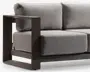 Nærbillede af en moderne sofa med tykke, lysegrå stofhynder på både sæde og ryg. Armlænet og bunden er lavet af robust metal med mat finish i en mørk taupe farve og har et geometrisk, åbent design. Hynderne ser bløde og aftagelige ud, hvilket giver en komfortabel siddeoplevelse.