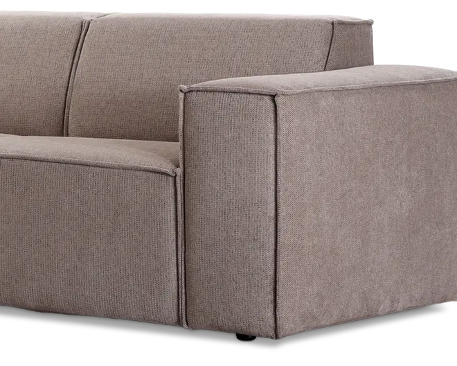 Nærbillede af et sofa-hjørne med tykke, firkantede armlæn og sædehynder. Betrækket er lavet af en tekstureret, lysebrun stof med synlige syninger langs kanterne, hvilket giver et moderne og struktureret udtryk. Sofaen har et minimalistisk design med rene linjer og en solid konstruktion.