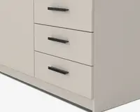 Nærbillede af en del af et møbel med tre skuffer, der har matte sorte, rektangulære greb. Overfladen er glat og har en lys beige eller offwhite farve. Skufferne er jævnt fordelt og har rene, moderne linjer, hvilket giver møblet et minimalistisk og moderne udtryk.