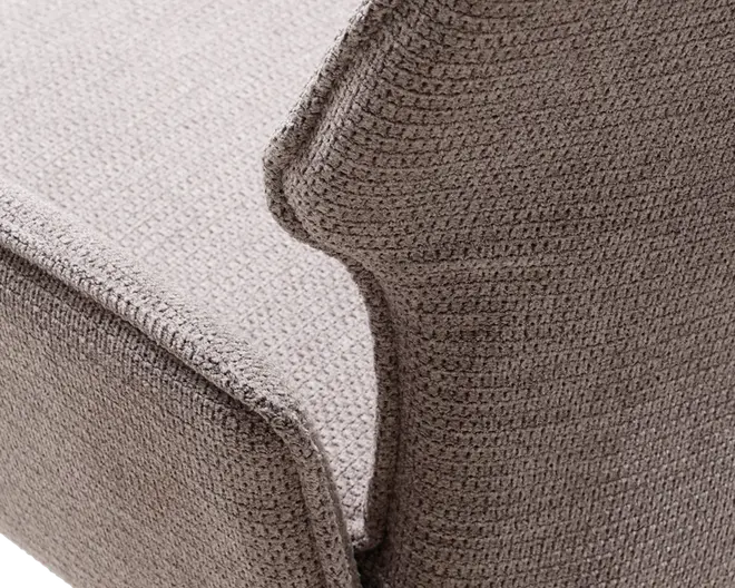 Nærbillede af et tekstureret stofbetræk i en neutral beige farve. Stoffet har et vaffellignende, ternet mønster og fremstår blødt og kraftigt, hvilket giver en hyggelig og komfortabel fornemmelse. Syningerne er synlige langs kanterne, hvilket indikerer forstærkede sømme for holdbarhed.