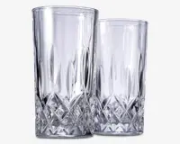 To høje, klare drikkeglas med et facetslebet diamantmønster i bunden, som giver et tekstureret og elegant udseende. Den øverste del af glassene er glat og cylindrisk, mens den nederste del har indviklet geometrisk detaljering for bedre greb og et flot visuelt udtryk.