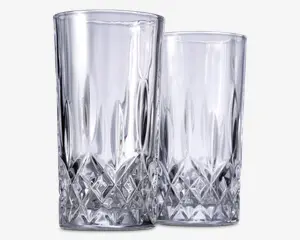 To høje, klare drikkeglas med et facetslebet diamantmønster i bunden, som giver et tekstureret og elegant udseende. Den øverste del af glassene er glat og cylindrisk, mens den nederste del har indviklet geometrisk detaljering for bedre greb og et flot visuelt udtryk.