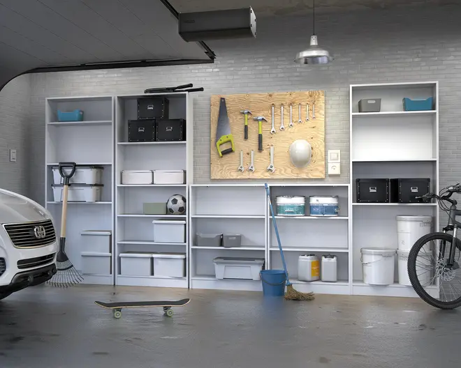 Hvide modulære reoler med flere åbne hylder, der indeholder forskellige opbevaringskasser, beholdere og bokse i forskellige størrelser og farver. Nogle hylder har sorte og hvide kasser med låg, mens andre har gennemsigtige plastkasser. Over de midterste hylder er der monteret en værktøjsplade med pænt organiseret håndværktøj som sav, hammer, skruenøgler, tang og en hjelm. Reolerne står op ad en grå murstensvæg, og gulvet foran er ryddet bortset fra et skateboard, en kost, en moppe med blå spand og en fodbold. Det samlede udtryk er rent, organiseret og funktionelt, velegnet til opbevaring i garage eller bryggers.