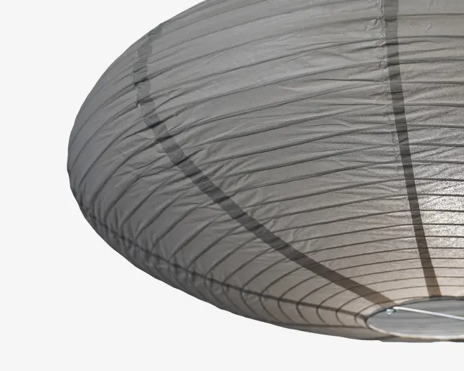 Stor, oval lampeskærm lavet af gennemsigtigt gråt stof med jævnt fordelte horisontale ribber og to lodrette mørke striber. Materialet spreder lyset blødt og giver en varm glød. Nederst er der en lille metalring, som giver struktur.