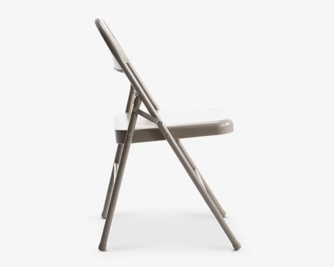 Sidevisning af en klapstol med metalstel og fladt sæde. Stolen har et enkelt, minimalistisk design med rørformede ben og et ryglæn, der flugter med sædet, når den er klappet sammen. Led og hængsler er synlige, hvilket viser stolens sammenklappelige funktion til nem opbevaring og transport.