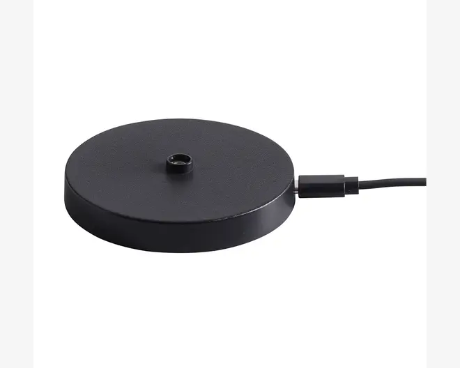 En rund, flad, sort base med mat overflade, der har et centralt gevindhul til montering. Basen er forbundet med et strømkabel på siden, hvilket indikerer, at den er elektrisk drevet eller giver elektrisk forbindelse. Designet er minimalistisk og moderne.