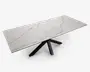 Rektangulært bord med en hvid bordplade med marmoreffekt og diskrete grå årer. Bordpladen består af tre paneler, hvilket indikerer et udtræksdesign. Bordets base har sorte, skråtstillede ben, der mødes i midten og giver et moderne og stabilt udtryk.