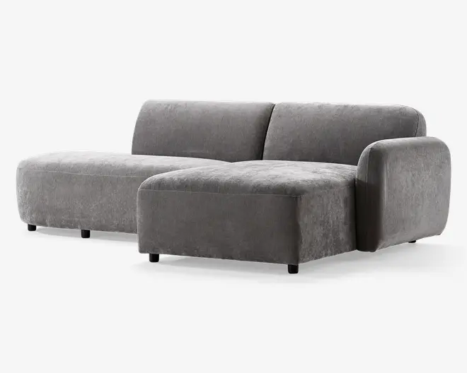 Moderne hjørnesofa med minimalistisk design, betrukket med blødt gråt stof. Sofaen har lav profil med brede, dybe sæder og én armlæn på højre side. Hynderne er tykke og bløde, hvilket giver god komfort. Benene er korte og diskrete, hvilket får sofaen til at se svævende ud. Perfekt til moderne stuer.