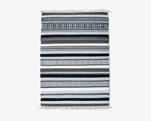 Rektangulært vævet tekstil med vandrette striber i sorte, hvide og grå nuancer. Striberne varierer i bredde og har forskellige mønstre som prikker, diamanter og ensfarvede linjer. Begge ender af tekstilet har korte, knyttede frynser.