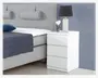 Et moderne, hvidt sengebord med blank overflade og tre skuffer uden greb. Skufferne har et minimalistisk, fladt frontdesign. Bordet er rektangulært med rene, lige kanter. Ovenpå står en hvid lampe med rillet struktur og sort lampeskærm samt en lille dekorativ plante i en glaspotte.