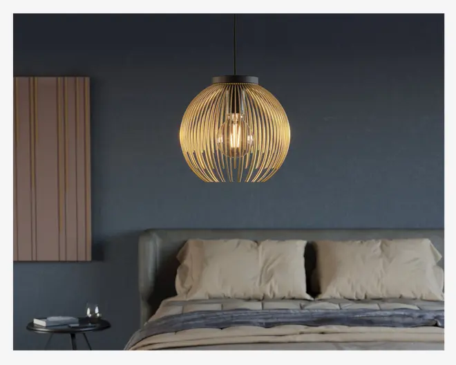 En moderne loftslampe med en kugleformet skærm lavet af jævnt fordelte, buede trælameller. Pæren er synlig gennem det åbne design, hvilket giver et varmt og hyggeligt lys. Lampen hænger i en sort ledning og er placeret over en seng med neutralt sengetøj i et moderne soveværelse.