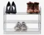 Trestykket skoreol i metal med kromfinish, der rummer tre par sko: sorte højhælede sko, brune læderstøvler og grå sportssko. Reolen har et åbent design med vandrette stænger på hver hylde, hvilket giver nem synlighed og adgang til skoene. Konstruktionen er let og kompakt, velegnet til organisering af fodtøj i små rum.