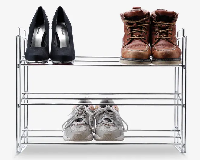 Trestykket skoreol i metal med kromfinish, der rummer tre par sko: sorte højhælede sko, brune læderstøvler og grå sportssko. Reolen har et åbent design med vandrette stænger på hver hylde, hvilket giver nem synlighed og adgang til skoene. Konstruktionen er let og kompakt, velegnet til organisering af fodtøj i små rum.