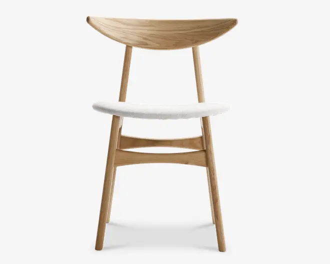 Stol med stel i lyst naturtræ, buet halvmåneformet ryglæn og let buet, hvidpolstret sæde. Benene er let skråtstillede for stabilitet, og der er en vandret støtte mellem for- og bagben for ekstra styrke. Designet er minimalistisk og moderne med bløde, afrundede kanter og et skandinavisk udtryk.