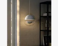 En moderne pendellampe med en kugleformet hvid skærm, der er indrammet af en cirkulær metalring i guld. Designet har et vandret guld bånd, som deler kuglen og giver et markant geometrisk udtryk. Lampen hænger fra en tynd guldfarvet ledning og udsender et varmt, stemningsfuldt lys, perfekt til moderne indretning.