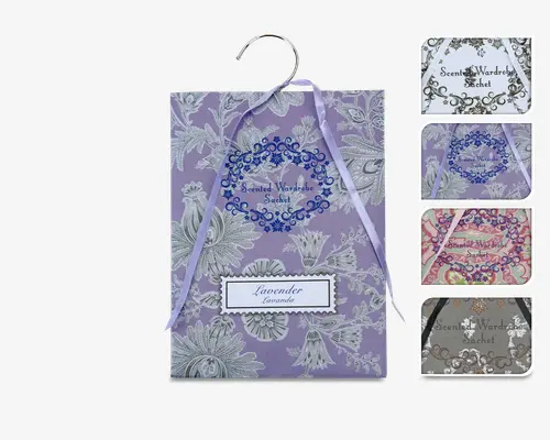 Dekorativ duftpose med blomsterprint, mærket med lavendelduft. Posen har en pastel lilla baggrund med hvide blomsterillustrationer, samt et bånd og en metalkrog til ophængning. Hovedposen vises i lilla, mens der til højre ses flere farve- og duftvarianter, herunder hvid, pink og grå, alle med detaljerede blomsterdesigns og matchende bånd.
