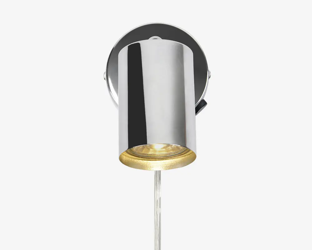 Væghængt lampe med cylindrisk form og blank kromfinish. Lampen har en rund base og en nedadrettet lyskilde med en klar linse i bunden. Designet er moderne og minimalistisk, velegnet til nutidige indretninger.