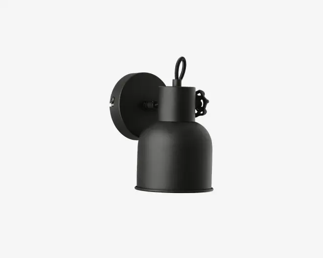 Væghængt lampe i mat sort finish med en rund, industrielt inspireret metalskærm. Lampen har en cirkulær base og en kort arm, der forbinder basen med skærmen. Skærmen er glat og let udvidet forneden, hvilket leder lyset nedad. Designet er minimalistisk og moderne.