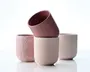 Sæt med fire minimalistiske, cylindriske kopper i bløde pastelfarver af rosa og beige. Hver kop har en glat, mat overflade med diskrete variationer i tekstur og farve, hvilket giver et håndlavet udtryk. Kopperne har lige sider med en let afrundet bund og ingen hank, hvilket gør dem velegnede til både varme og kolde drikke. Designet er moderne og elegant, perfekt til et nutidigt borddækning.