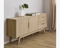 Lys egetræsskænk med minimalistisk design, to centrale låger med indbyggede greb og tre skuffer til højre. Skænken står på skråtstillede, koniske ben og har en glat, naturlig træfinish. Toppen er dekoreret med en hvid vase med grønne blade og to stabelde bøger.