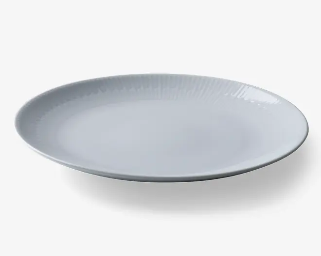 Rund, hvid tallerken med let hævet kant og diskrete teksturerede linjer, der stråler ud fra midten mod kanten. Overfladen er glat og blank, hvilket giver et rent og moderne udtryk.