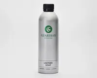 En høj, cylindrisk sølvfarvet flaske med sort skruelåg. Flasken har et grønt 'G'-logo og mærket 'Guardian Furniture Care' trykt i grønt. Nederst på etiketten står der 'Leather Soap' med fed sort skrift, og derunder er der oversættelser på flere sprog. Designet er stilrent og moderne med en metallisk overflade.