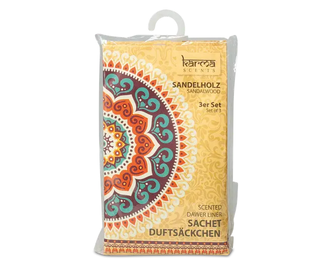 Rektangulær pakke med et livligt mandala-design i orange, turkis og hvid på en gul baggrund. Emballagen er indpakket i klar plast og har en ophængningsløkke øverst. Teksten på forsiden angiver, at produktet er et sæt med tre duftende skuffeindlæg med sandeltræduft. Udseendet er dekorativt og farverigt med et boheme-inspireret mønster.