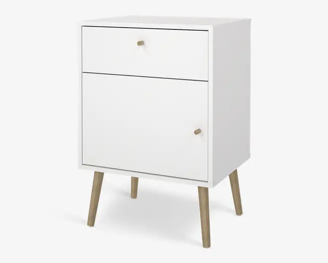 Et kompakt, moderne skab med mat hvid finish, der har en øverste skuffe og et nederste skabsrum med låge. Både skuffen og lågen har små, runde knopper i lyst træ. Skabet står på fire skråtstillede ben i lyst træ, hvilket giver det et udtryk i retro stil.