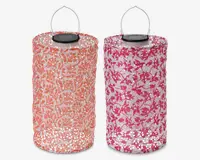 To cylindriske lanterner med metalhåndtag og solpaneler på toppen. Den venstre lanterne har et orange og hvidt bladmønster, mens den højre har et pink og hvidt blomstermønster. Begge lanterner har perforerede overflader, der lader lyset skinne igennem de dekorative mønstre.