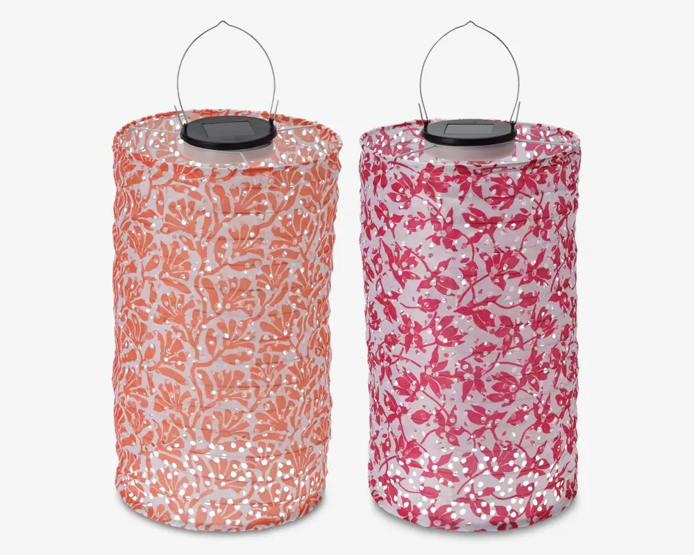 To cylindriske lanterner med metalhåndtag og solpaneler på toppen. Den venstre lanterne har et orange og hvidt bladmønster, mens den højre har et pink og hvidt blomstermønster. Begge lanterner har perforerede overflader, der lader lyset skinne igennem de dekorative mønstre.