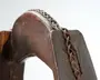 Nærbillede af et mørkt, vejrslidt træstykke med en buet udskæring og en ældet metalkæde lagt langs overkanten; overfladen har tydelige slidmærker, ridser og en rustfarvet patina.