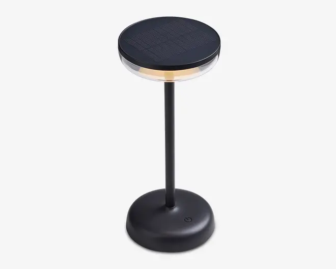 En moderne, sort bordlampe med rund fod og en slank, lodret stang. Lampen har en cirkulær top med solpaneloverflade, en gennemsigtig ring under toppen for blødt lys og en touch-tænd/sluk-knap på foden. Designet er stilrent og minimalistisk, velegnet til moderne indretning.