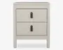Et moderne, rektangulært natbord med en glat, mat lysebeige finish. Det har to rummelige skuffer, hver med en enkelt lodret læderstrop som greb i midten, dekoreret med en messingnitte. Designet er minimalistisk med rene linjer og let tilspidsede ben, hvilket giver et moderne udtryk.