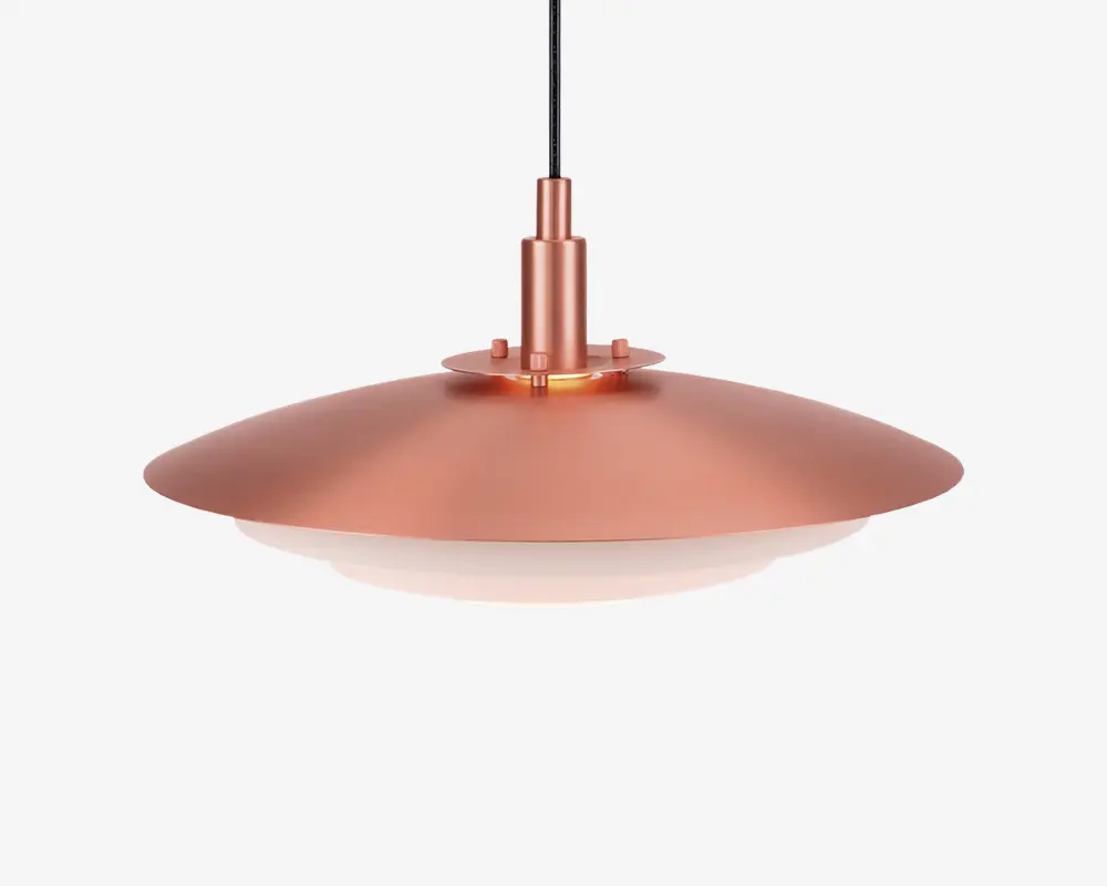 En moderne pendellampe med en bred, flad og cirkulær skærm i metallisk kobberfinish. Skærmen har en glat overflade og skråner let nedad, med en hvid diffuser i bunden for blød og jævn lysfordeling. Lampen hænger i en sort ledning og har et stilrent, minimalistisk design, der passer til moderne indretning.