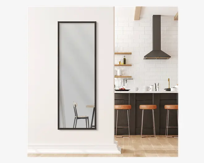 Højt, rektangulært spejl med en smal sort metalramme, monteret lodret på en hvid væg. Spejlet har et minimalistisk design og giver fuld længde refleksion. Rammen er tynd og moderne, hvilket giver et stilrent udtryk, der passer til moderne indretning.