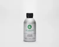 En sølvfarvet flaske med sort skruelåg, der har et grønt 'G'-logo og mærket 'Guardian Furniture Care' på etiketten. Etiketten angiver tydeligt 'Leather Cleaner' med fed sort skrift. Flasken har et enkelt, moderne design og ser ud til at være lavet af metal eller metallisk plast.