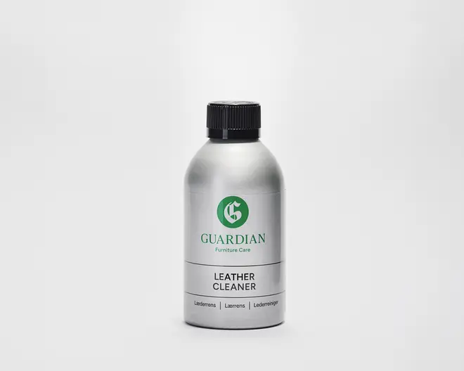 En sølvfarvet flaske med sort skruelåg, der har et grønt 'G'-logo og mærket 'Guardian Furniture Care' på etiketten. Etiketten angiver tydeligt 'Leather Cleaner' med fed sort skrift. Flasken har et enkelt, moderne design og ser ud til at være lavet af metal eller metallisk plast.