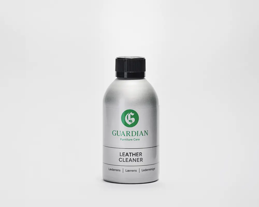 En sølvfarvet flaske med sort skruelåg, der har et grønt 'G'-logo og mærket 'Guardian Furniture Care' på etiketten. Etiketten angiver tydeligt 'Leather Cleaner' med fed sort skrift. Flasken har et enkelt, moderne design og ser ud til at være lavet af metal eller metallisk plast.