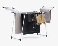 Sammenklappeligt tørrestativ med robust metalramme og flere vandrette stænger til ophængning af tøj. Stativet har to udtrækkelige vinger på hver side for ekstra tørreplads og er vist med håndklæder i forskellige farver og størrelser. Foden har plastikbeskyttelse for stabilitet og for at undgå ridser på gulvet.